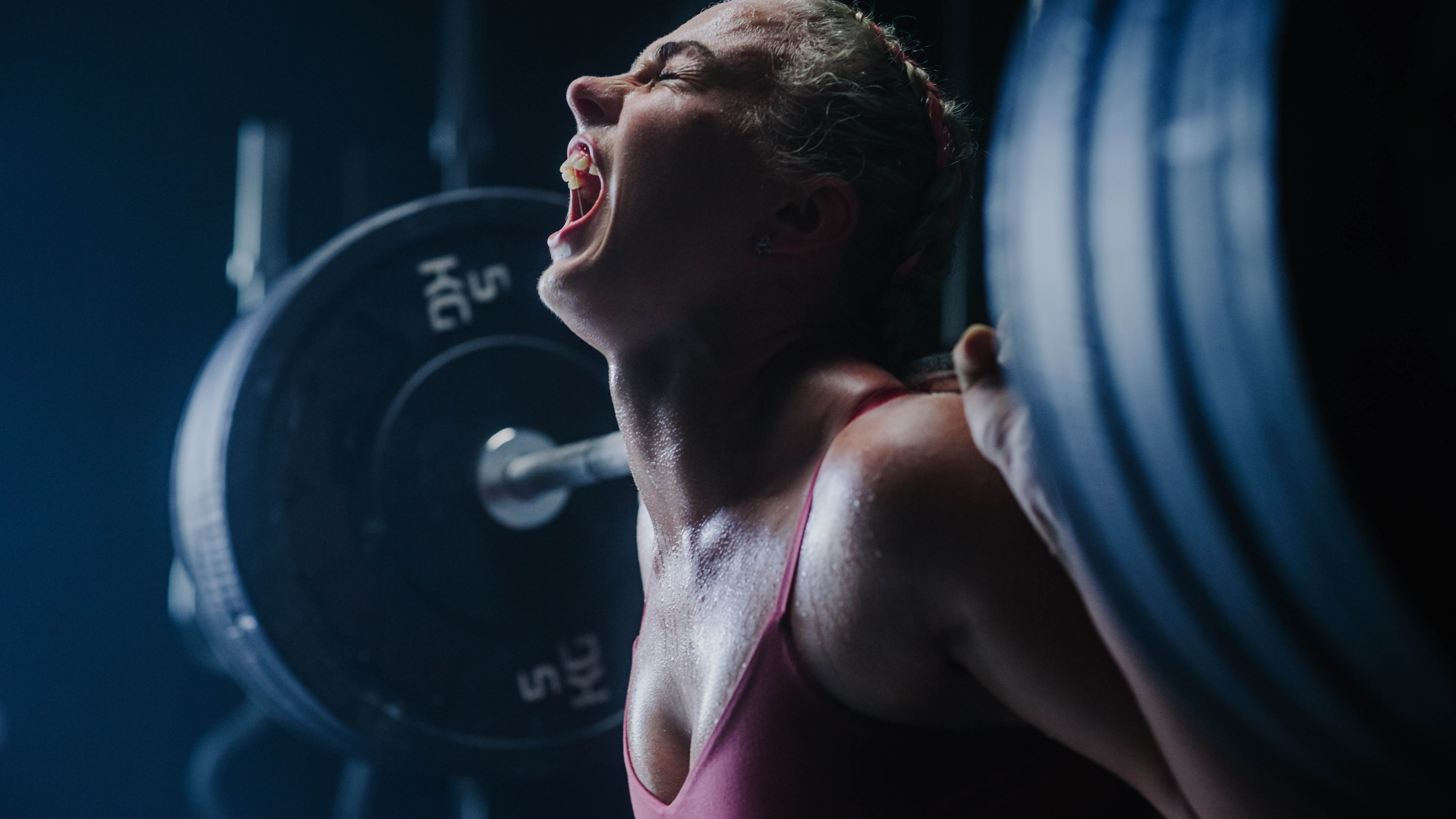 Young woman doing a deadlift with her head tilted back and yelling to the gym ceiling